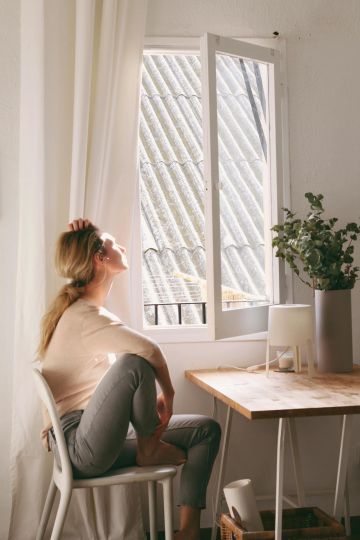 Frau blickt aus dem Fenster in die sonnige Umgebung