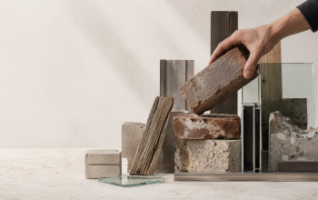 arrangierte wiederverwendete Baustoffe auf neutralem Hintergrund, alte Ziegel, Holzstücke, Glas, Metallprofile und Betonbruch. eine Hand hält prüfend einen alten Ziegel