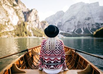 Frau von Hinten auf einem Ruderboot in idyllischer Landschaft sitzend