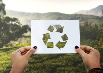 Hände halten das Recycling-Symbol vor einer idyllischen Landschaft