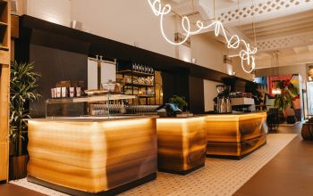 Eine moderne Kaffeebar mit warm beleuchteten Tresen und eleganter Inneneinrichtung, einschließlich Pflanzen und einer kunstvollen Beleuchtung.