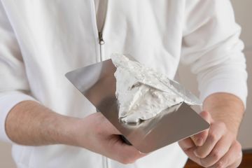 Kalkputz im Bad verarbeiten – das ist zu beachten: zu sehen ist der Oberkörper eines Mannes, der einen Spachtel mit weißer Kalk-Spachtelmasse hält.