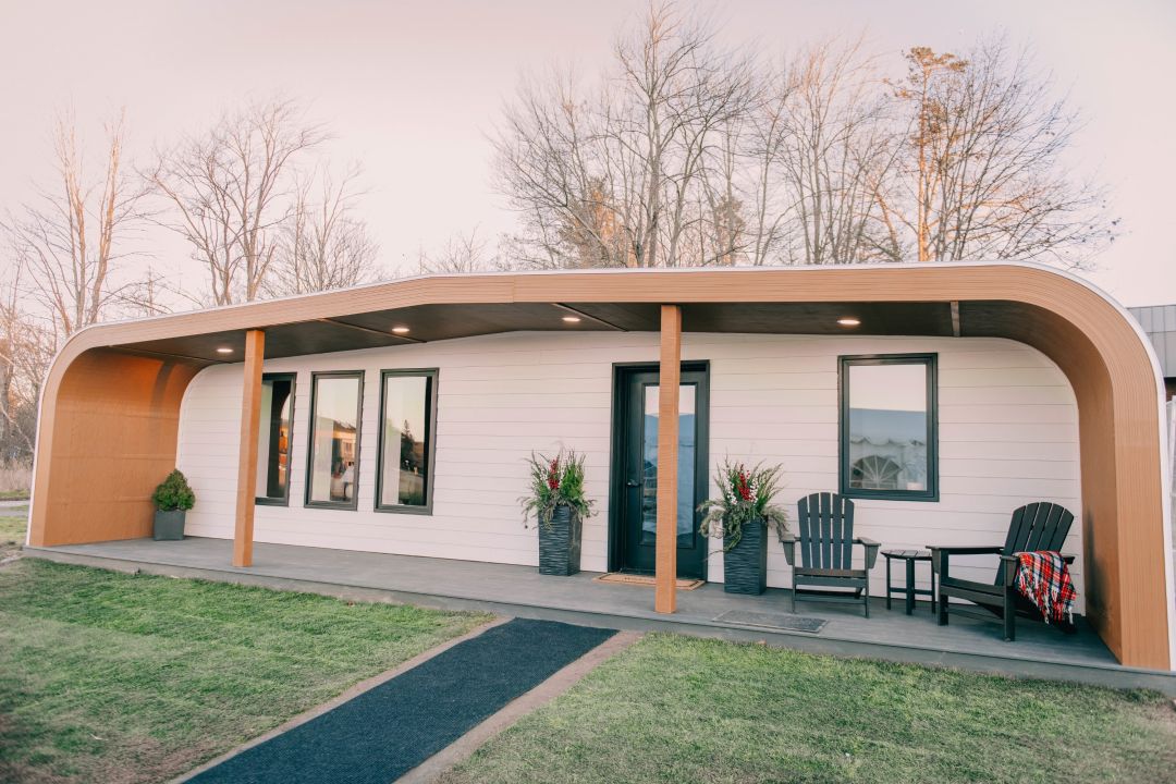 Ein modernes Haus mit geschwungenem Dach und einer Veranda, das teilweise mit 3D-Drucktechnologie gebaut wurde.