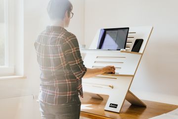 Gesund Arbeiten: ergonomische Büromöbel. Zu sehen ist eine Frau, die im Stehen an ihrem Laptop arbeitet.