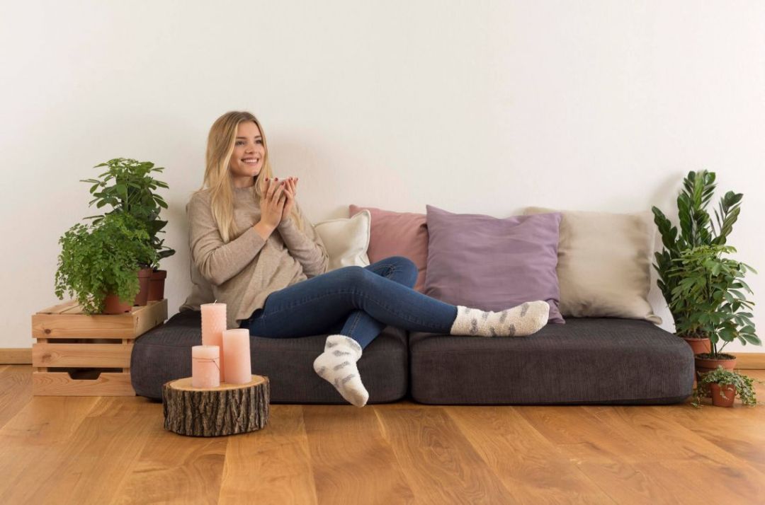 Frau sitzt auf Sofa, hinter ihr eine Lehmwand