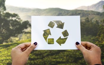 Hände halten das Recycling-Symbol vor einer idyllischen Landschaft