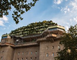 Der begrünte Bunker in Hamburg mit mehreren Etagen, umgeben von Bäumen, vor einem blauen Himmel.