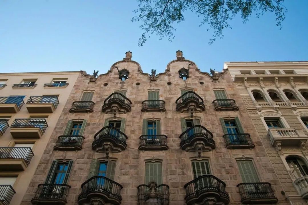 Die Fassade der Casa Calvet in Barcelona mit dekorativen Balkonen und kunstvollen Details, das sich gegen einen klaren Himmel abhebt.