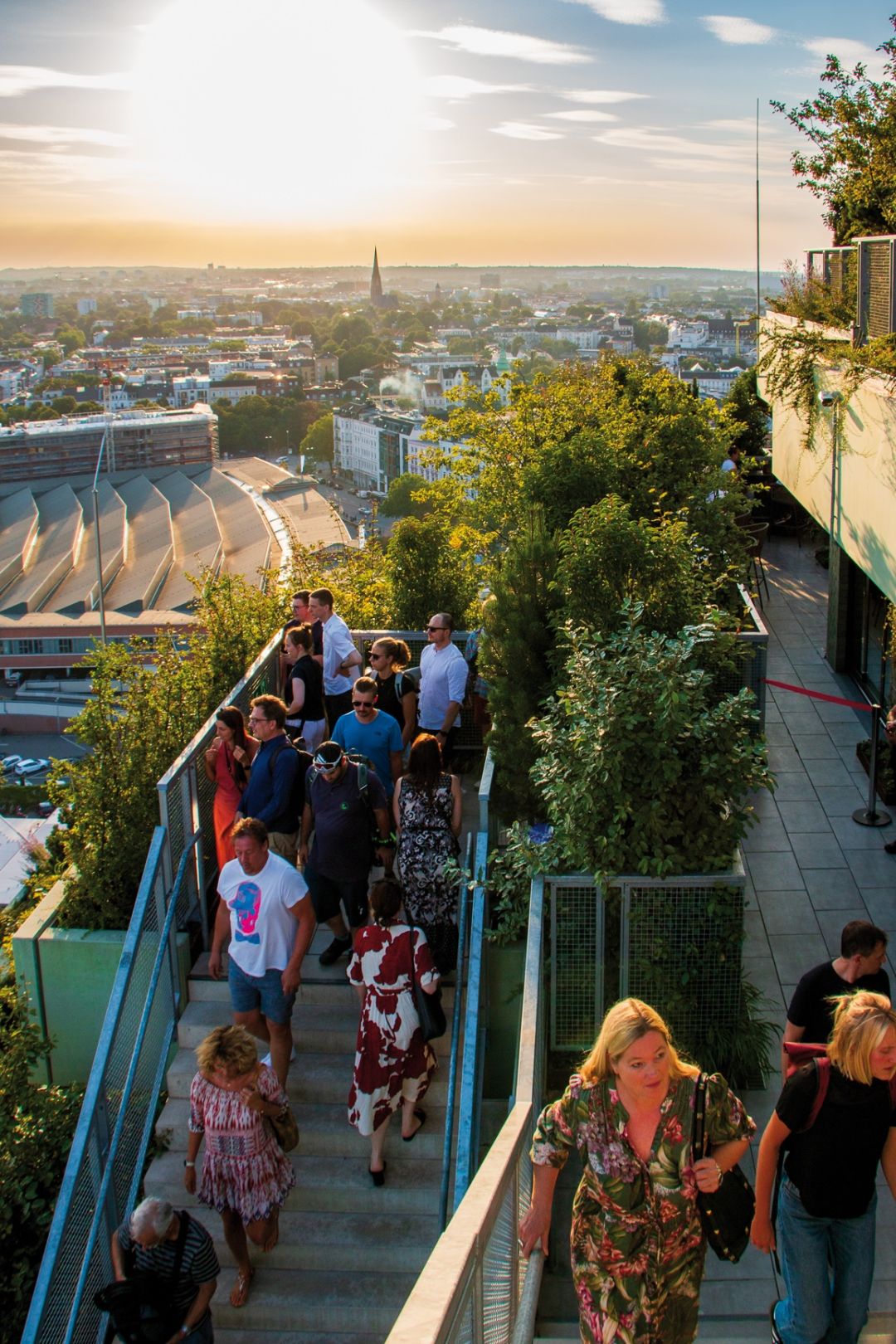 Menschen steigen eine Treppe auf einem begrünten Gebäude hinauf und genießen den Ausblick auf die Stadt.