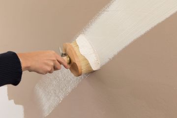 Vorteile und Nachteile von Lehm- und Kalkputz: zu sehen ist eine Hand mit Pinsel, die eine Wand mit Lehmfarbe streicht