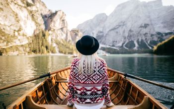 Frau von Hinten auf einem Ruderboot in idyllischer Landschaft sitzend