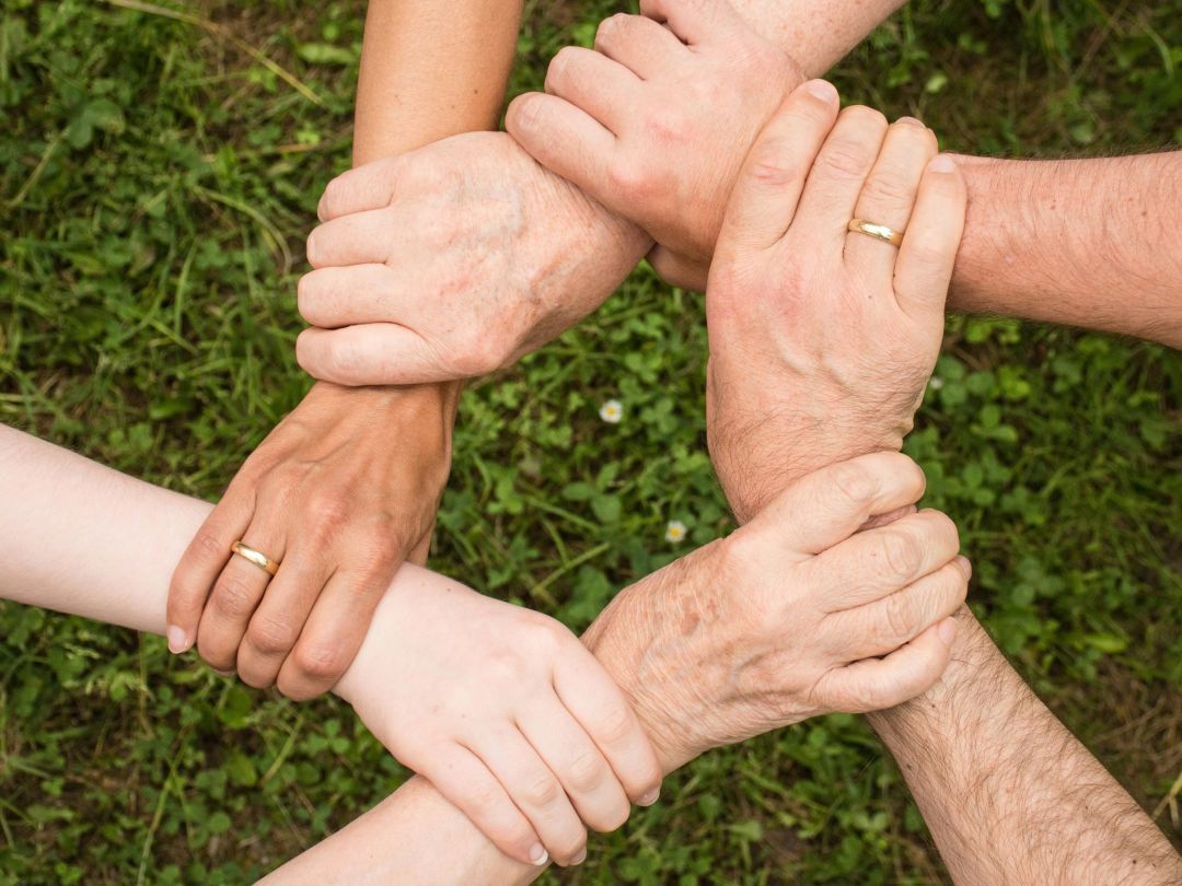 Sechs Hände fassen sich an und bilden einen Kreis. Symbol für Zusammenarbeit.